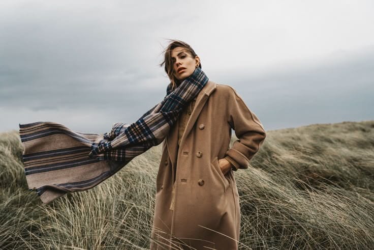 Pessoa a usar um casaco de lã camel e cachecol xadrez, ilustrando o posicionamento de uma marca de moda lifestyle.