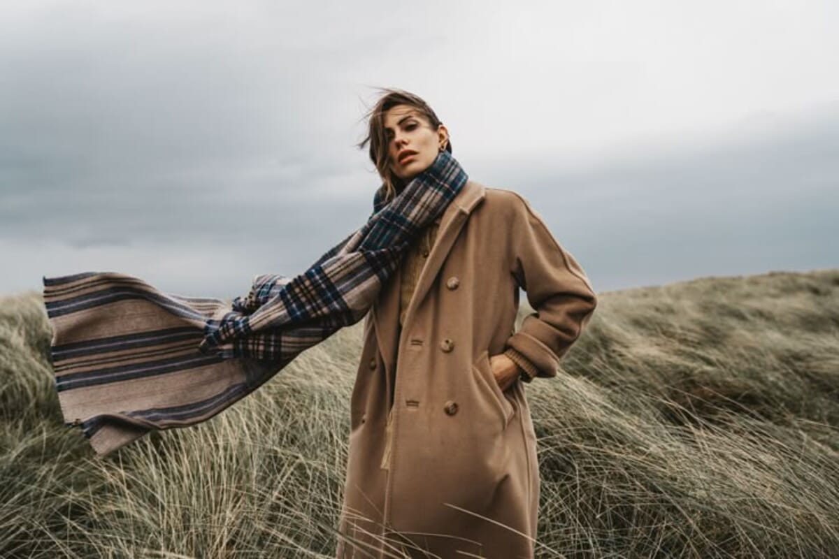 Editorial de inverno com sobretudo de lã camel e cachecol axadrezado em paisagem de dunas