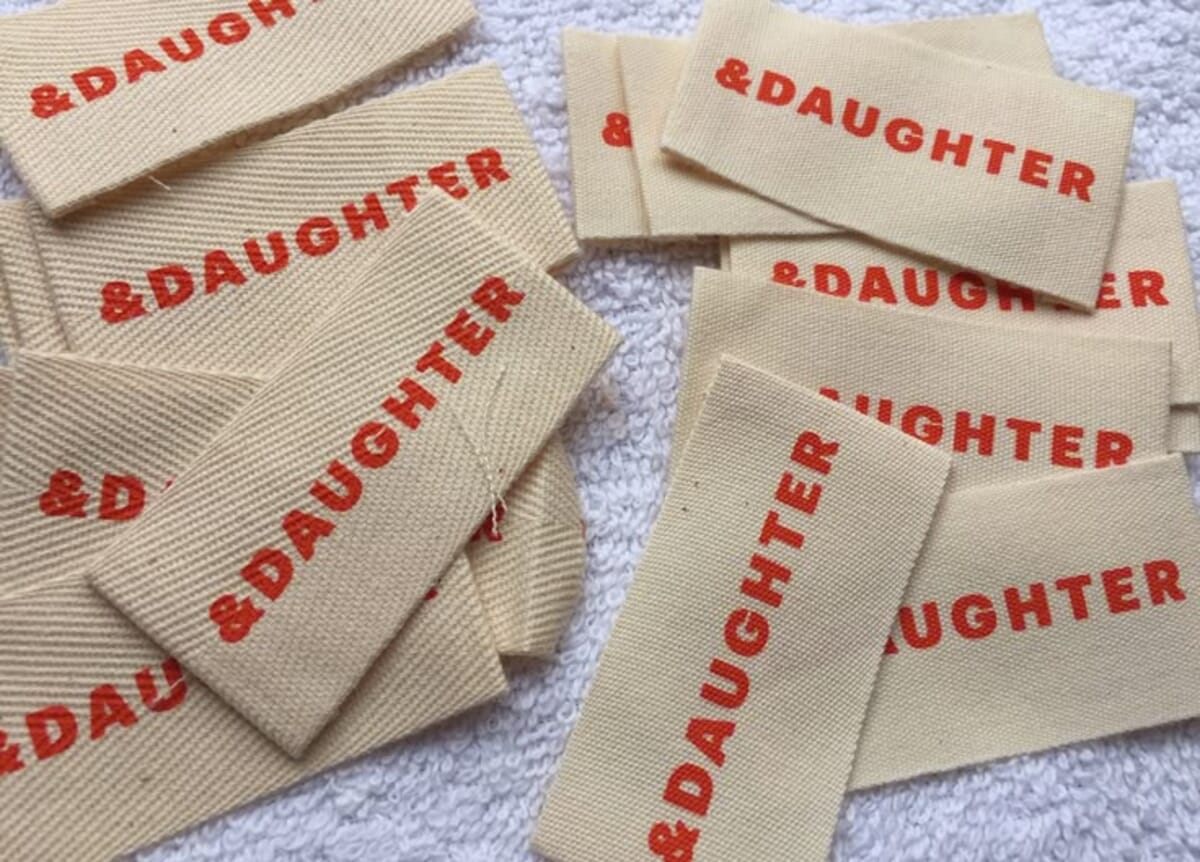 Flat-lay of garment trims, YKK zipper, horn buttons, woven main label, care label, hangtag with cotton string