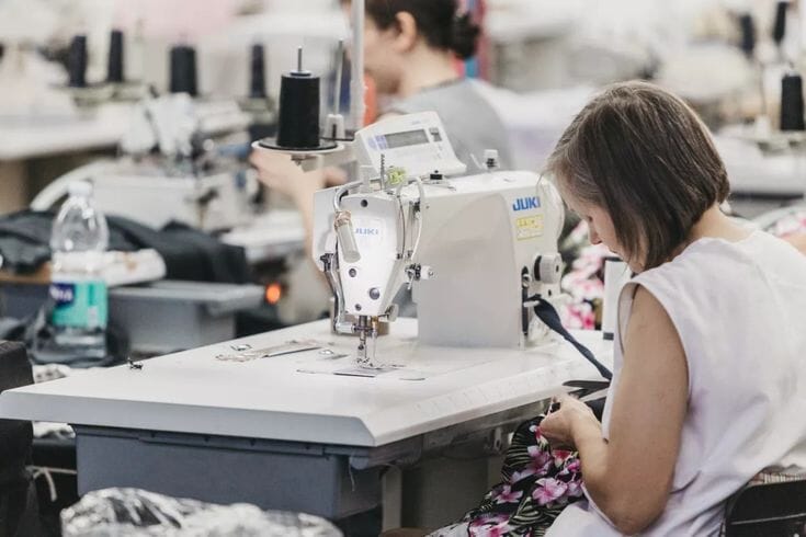 Roll of indigo denim fabric on a cutting table in a Portuguese textile factory, with wash samples displayed alongside.