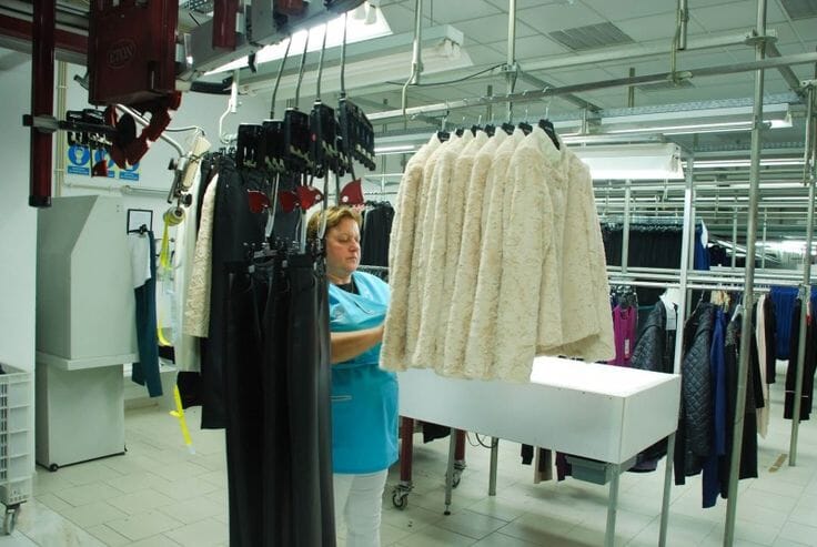 Worker inspecting finished garments hanging on rails