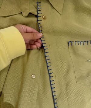 Hand blanket stitch along the edge of a woven jacket