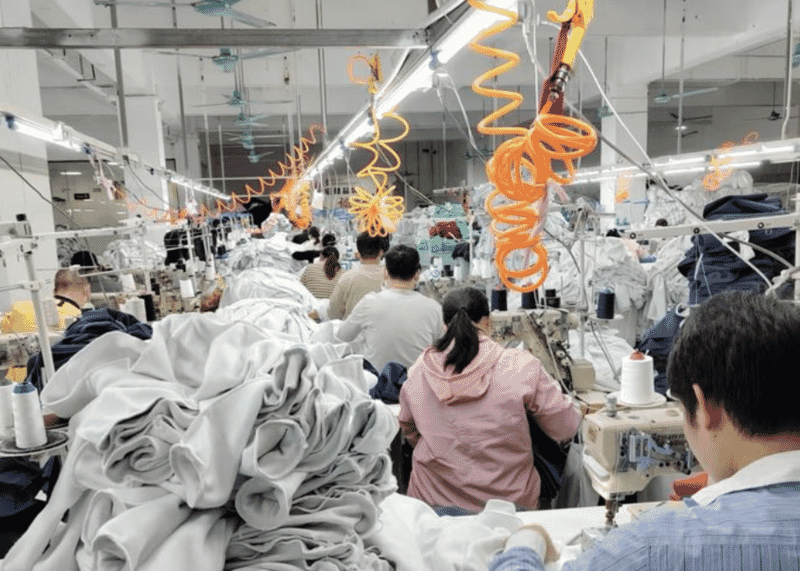 Sewing operators at a line of machines with stacks of grey fleece panels