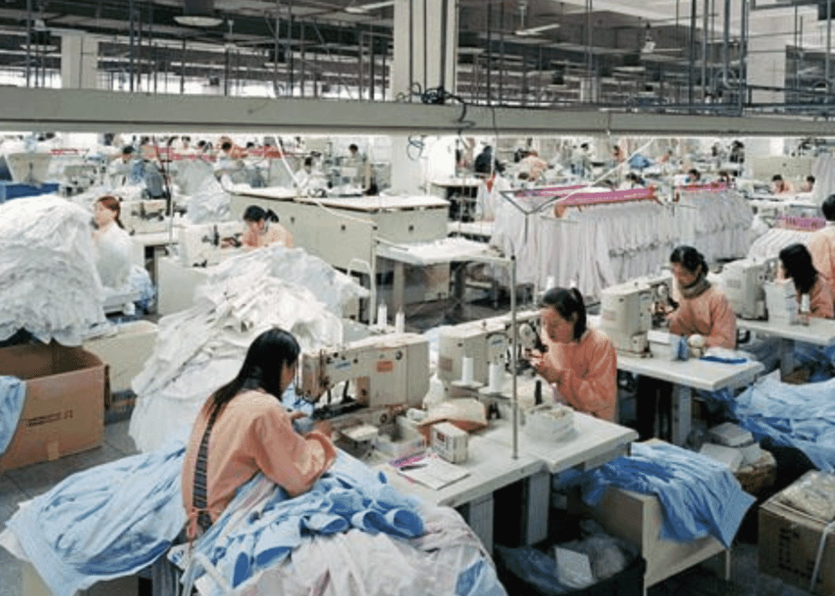 Machinists sewing light blue garments in a large factory hall