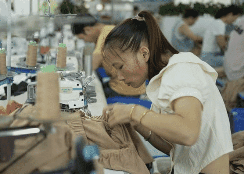 Close view of an operator sewing a beige knit panel on an overlock machine