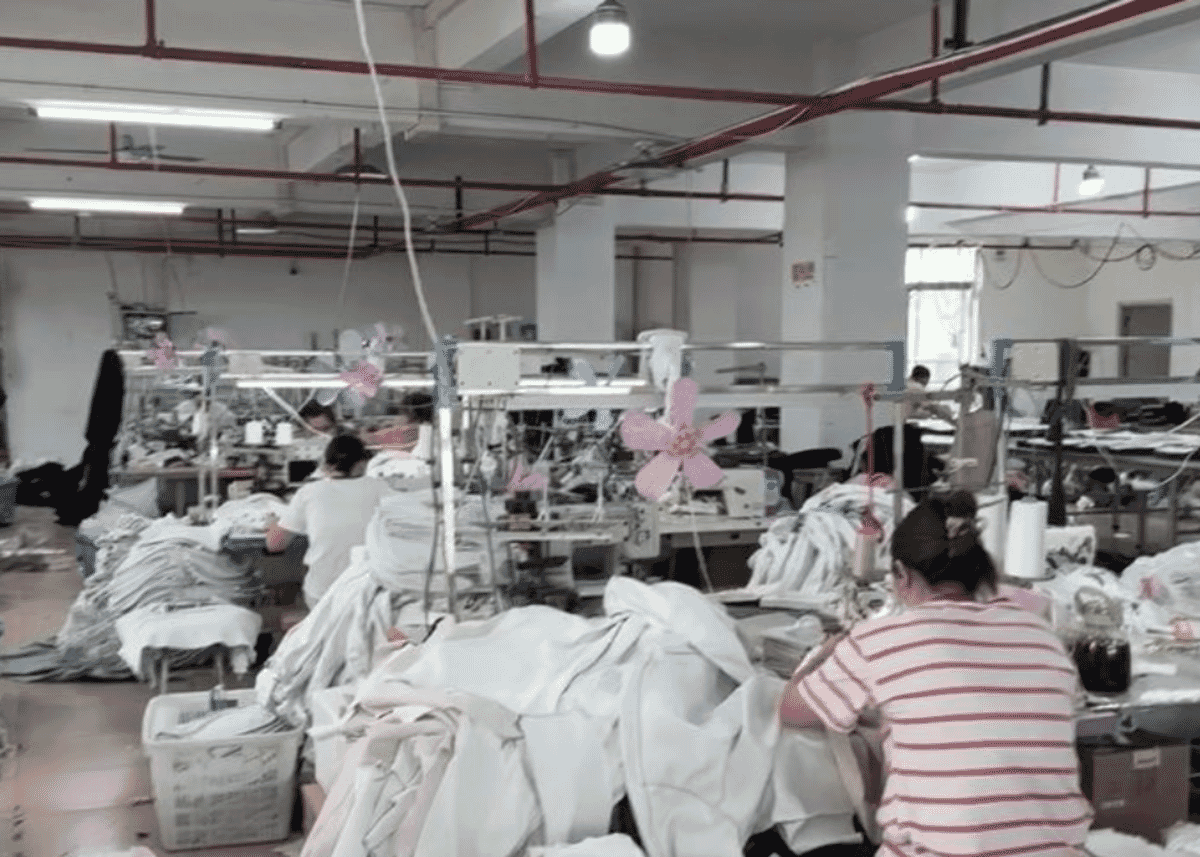 Machinists sewing white garments on a busy factory floor