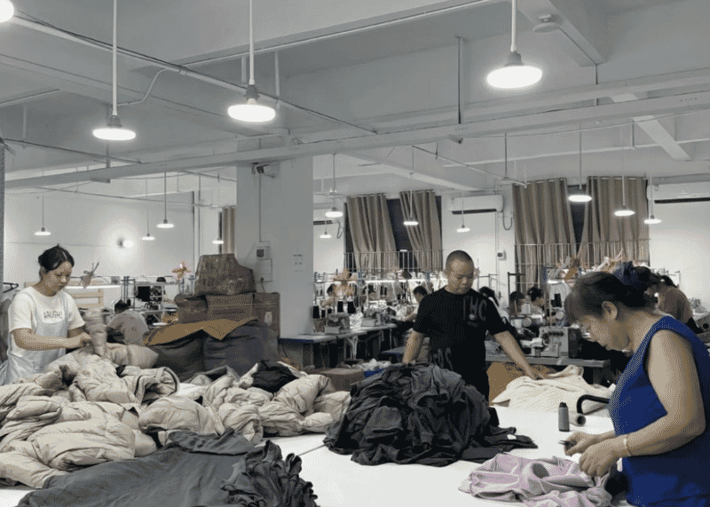 Workers trimming and folding padded and knit garments on a long table