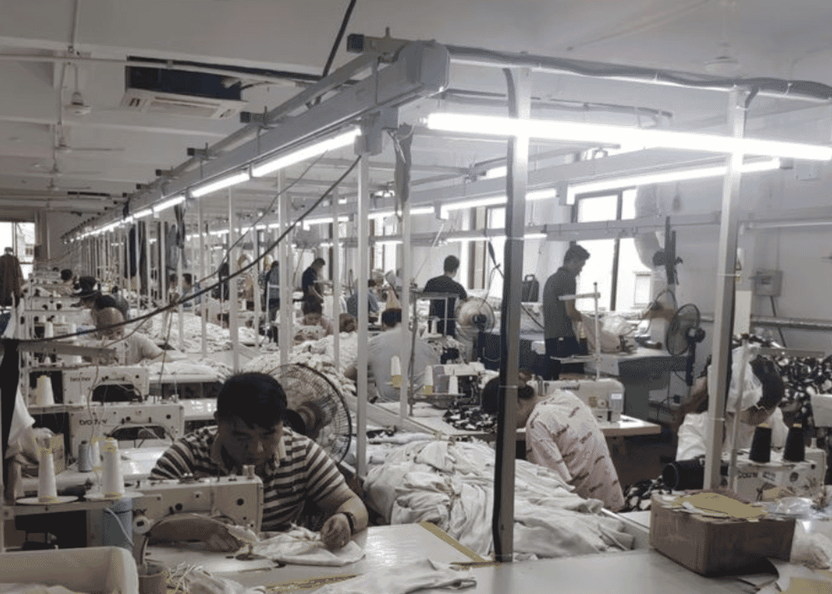 Long sewing floor with machinists at their stations under strip lights