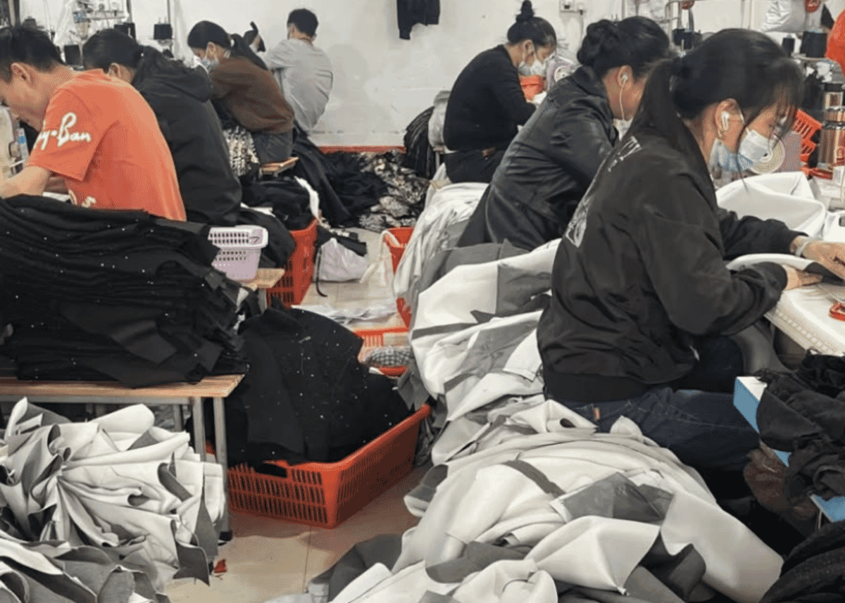 Machinists sewing dark knitwear at their tables with cut panels piled beside them