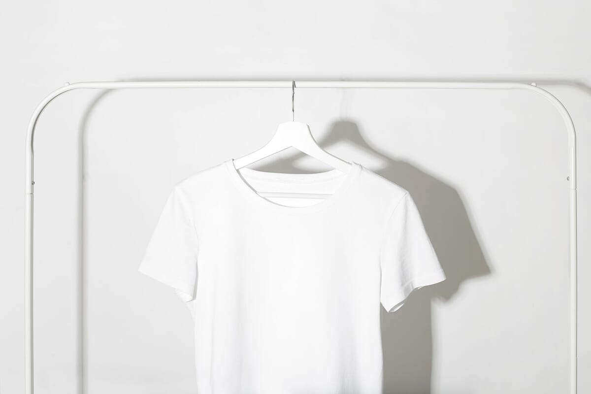 A plain blank white cotton crew-neck t-shirt hangs on a hanger against a clean studio wall