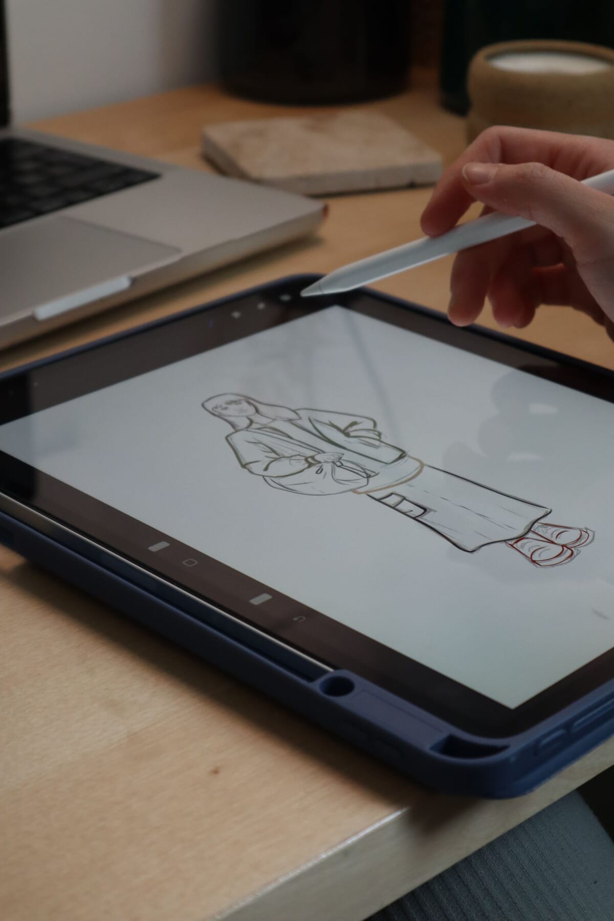 A designer's hand sketching a garment on a digital tablet with a stylus, drawing technical fashion flats