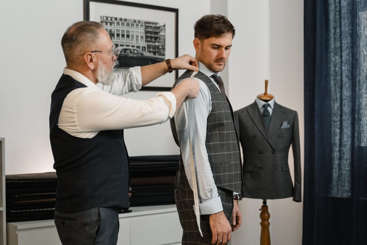A tailor measuring a garment with a tape measure to capture points of measure