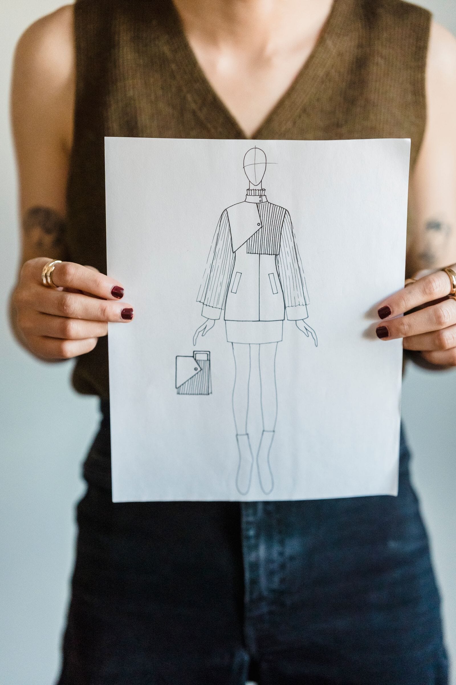 Woman holding up a pencil drawing of a jacket and trousers on a sheet of paper