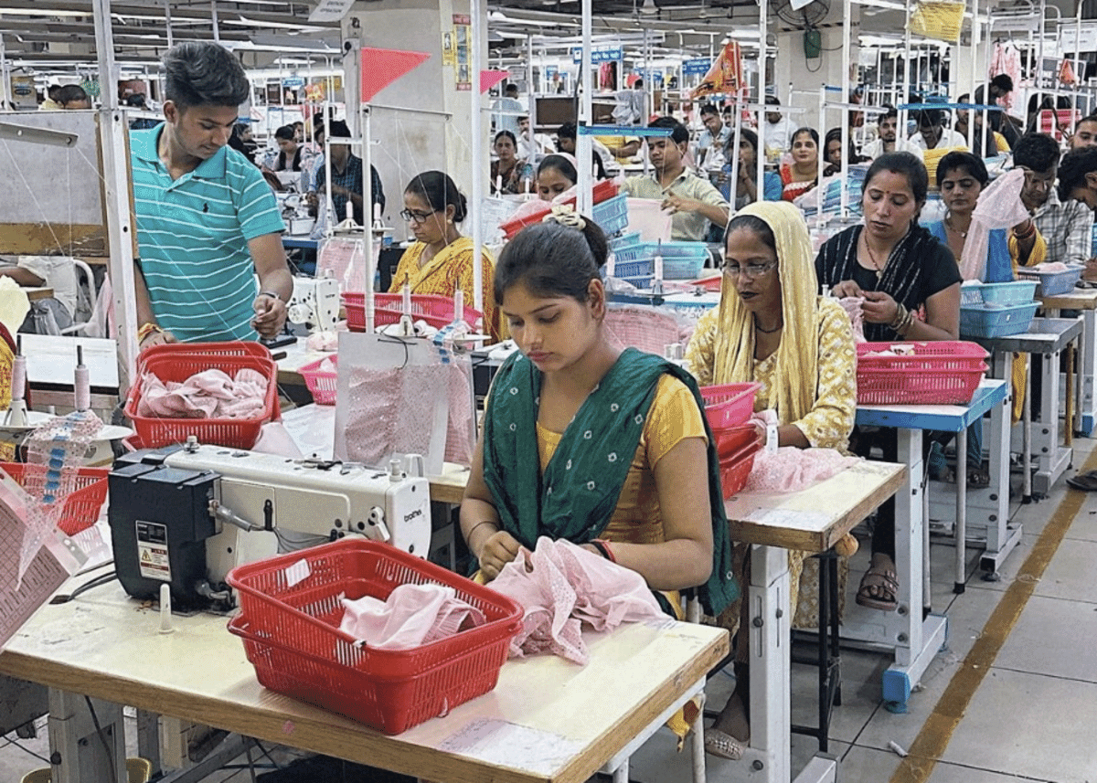 Sewing line with operators working on pink knit garments and red bundle baskets at each machine