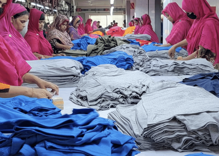 Women in pink headscarves sorting stacks of blue and grey knit garments on long tables