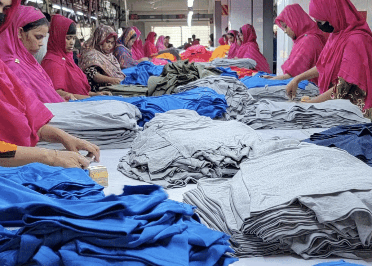 Women in pink headscarves sorting stacks of blue and grey knit garments on long tables