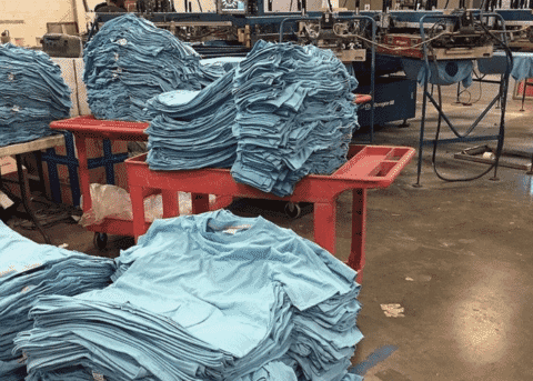 Stacks of finished light blue t-shirts on tables waiting for inspection