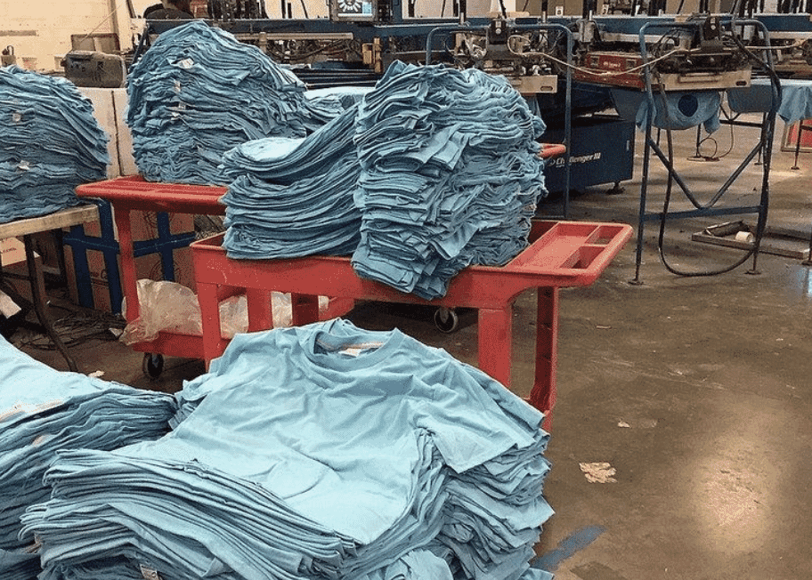 Stacks of finished light blue t-shirts on tables waiting for inspection