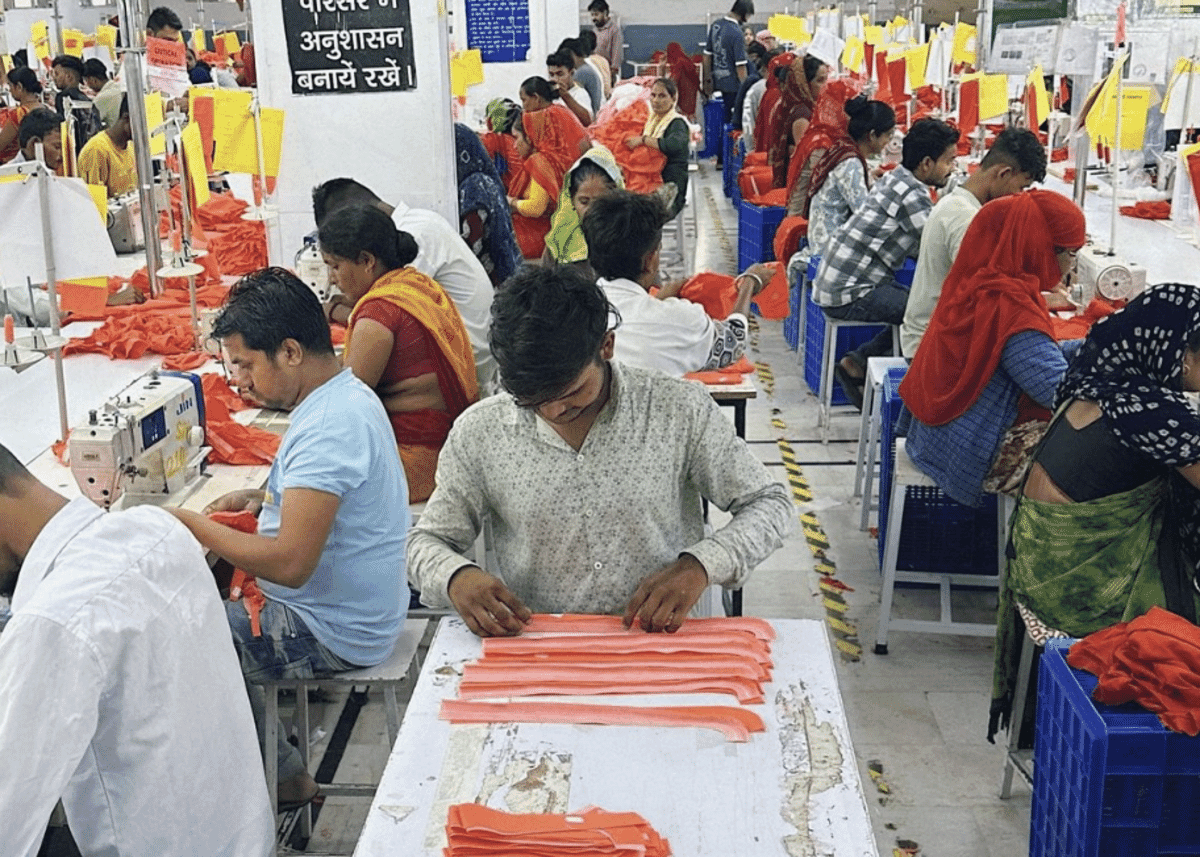 Sewing floor with workers handling orange cut panels and blue crates