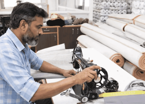A sample maker at a hand-wheel sewing machine beside rolls of fabric