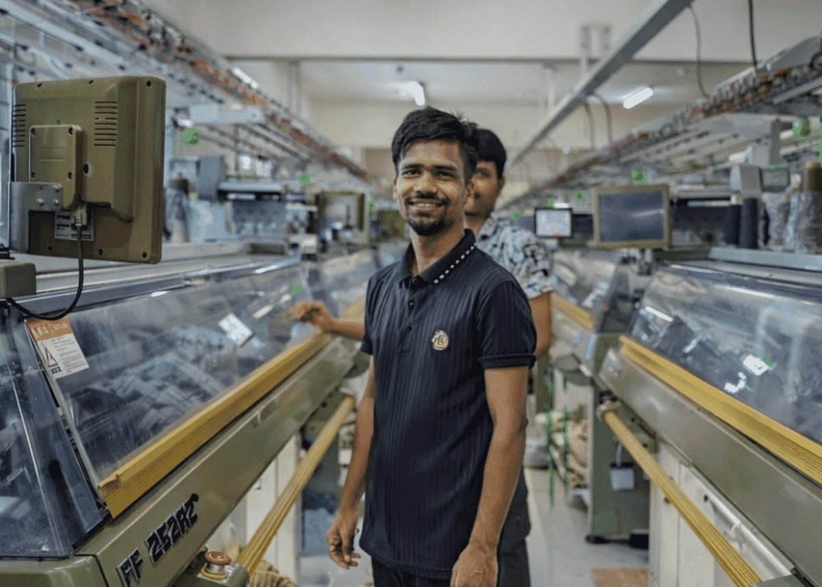 Smiling technician standing between rows of computerised flat knitting machines