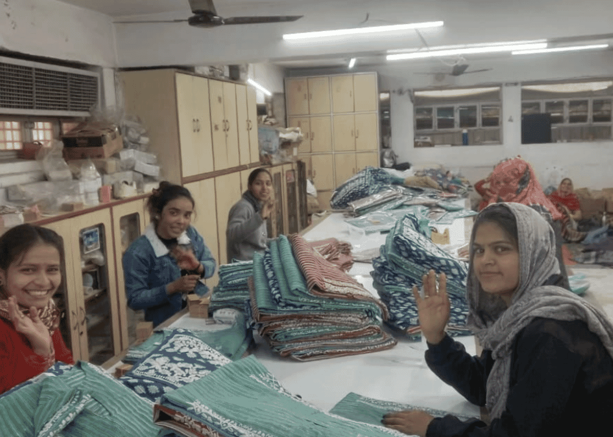 Women sorting stacks of printed fabric on a long table in a workshop