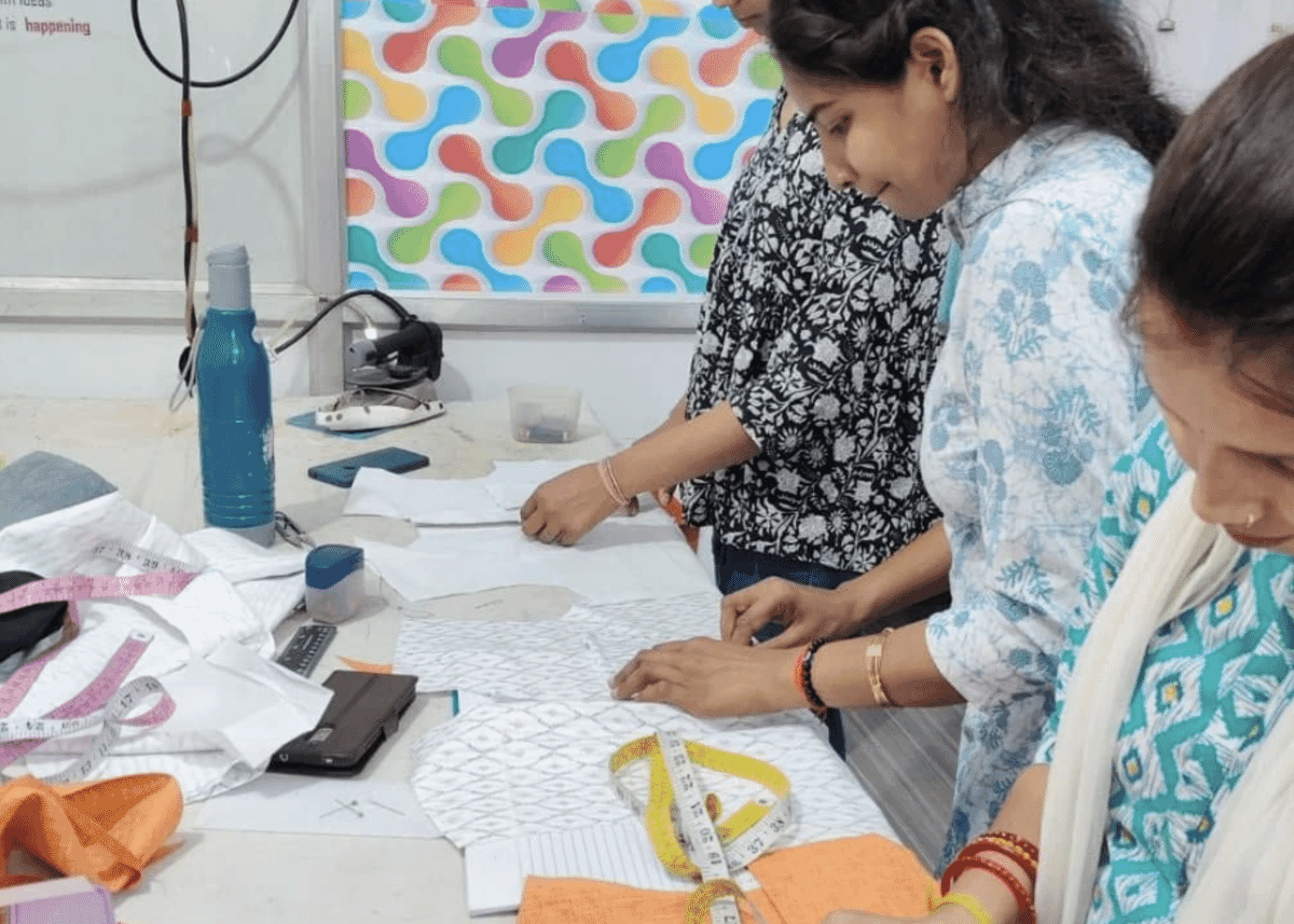 Women marking fabric with paper patterns and a tape measure on a work table