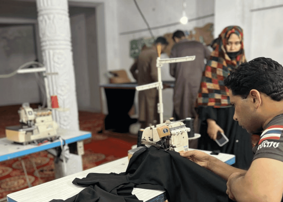 An operator overlocking a dark garment on a small workshop line