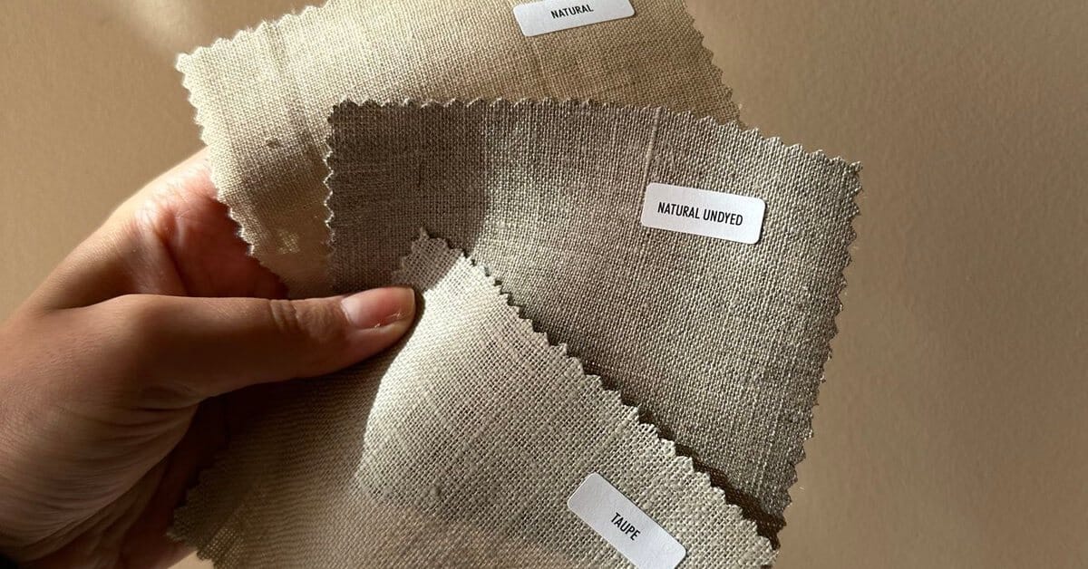 Hand holding three linen fabric swatches labelled natural, natural undyed and taupe