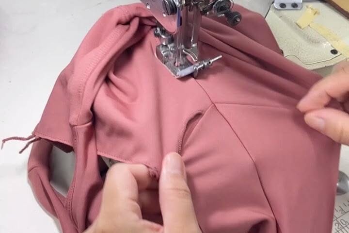 Mãos a guiar uma peça de malha elástica rosa sob o calcador de uma máquina de costura industrial