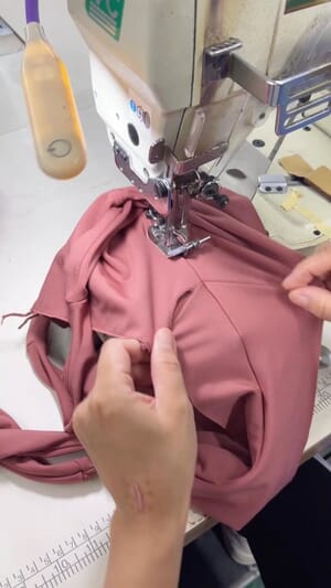 Hands feeding pink stretch fabric through a sewing machine