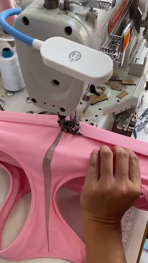 Hands guiding a pink sports bra through a flatlock machine