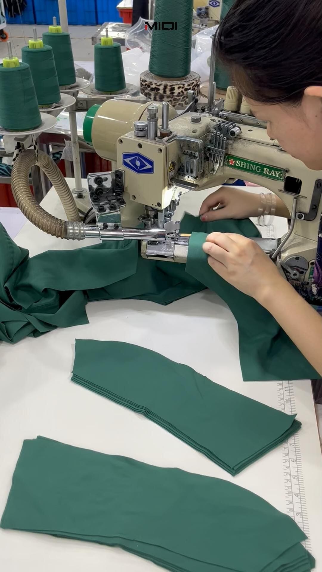 Operator feeding green stretch-knit panels through a flatseam sewing machine