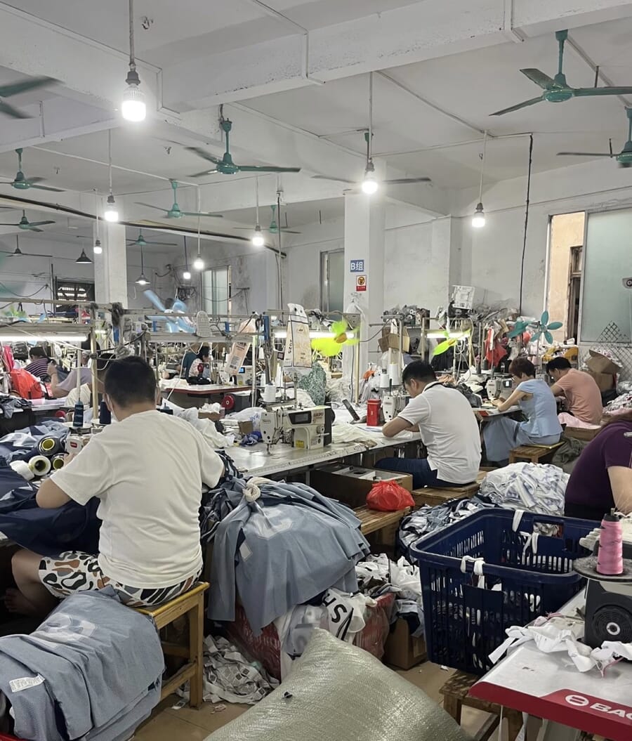 Busy sewing room with operators working through grey and white knit pieces and blue crates