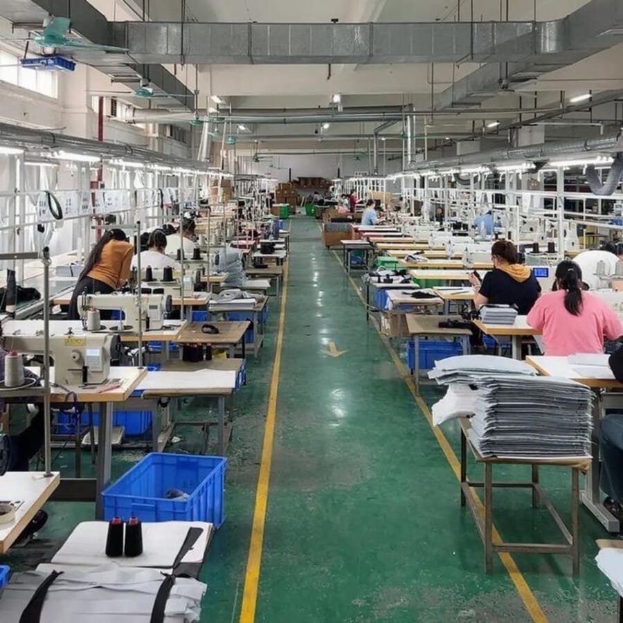 Long production aisle with a green floor, sewing stations and stacks of cut panels