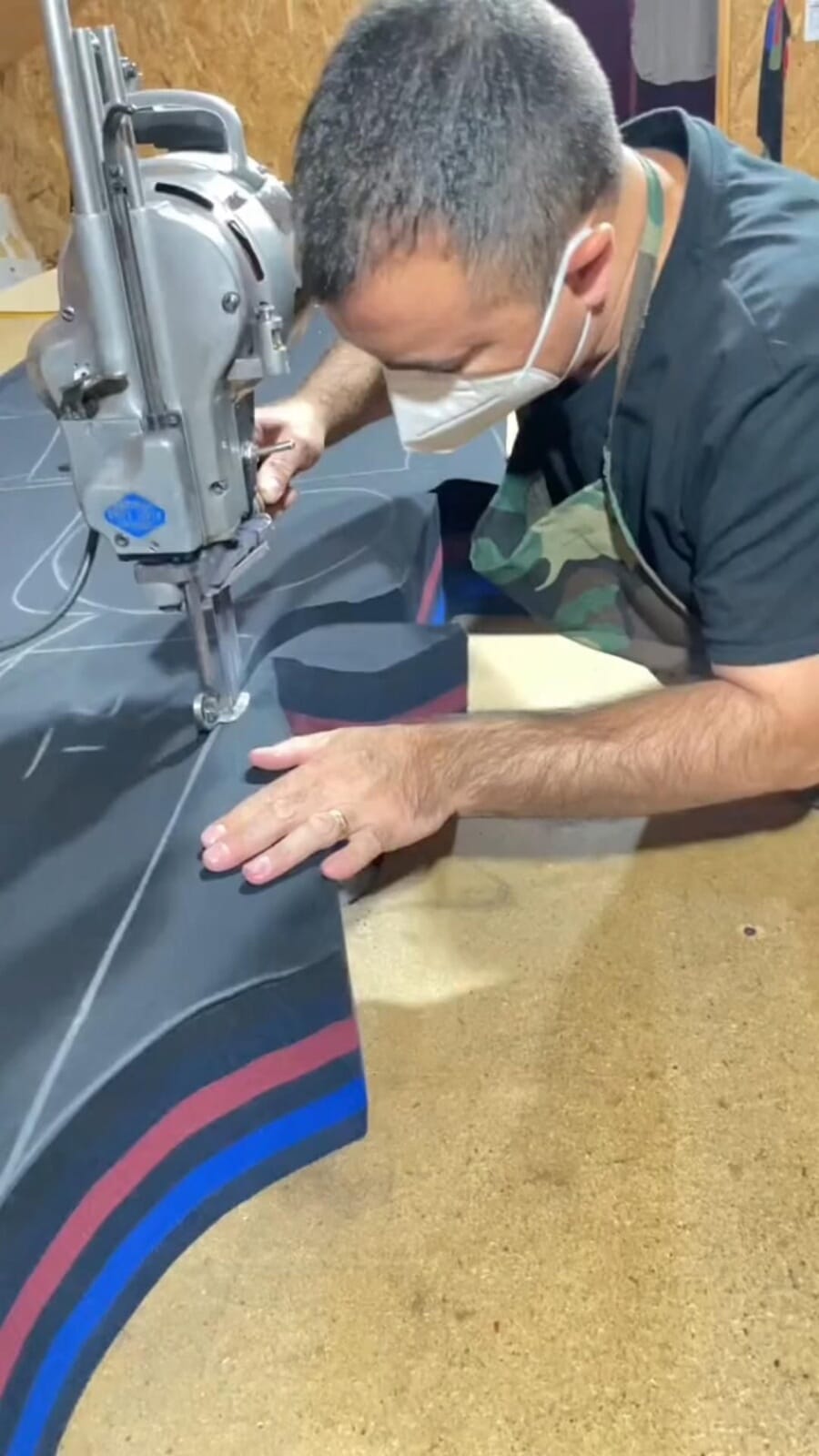 Cutter in a mask guiding a straight knife through stacked layers of dark fabric