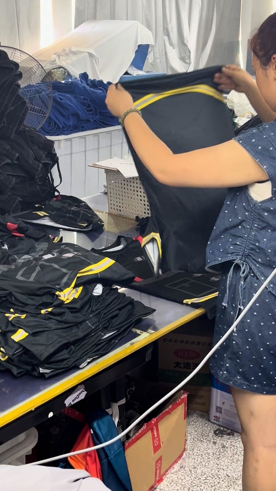 Measuring a black jacket with a tape, with finished jackets stacked on the table