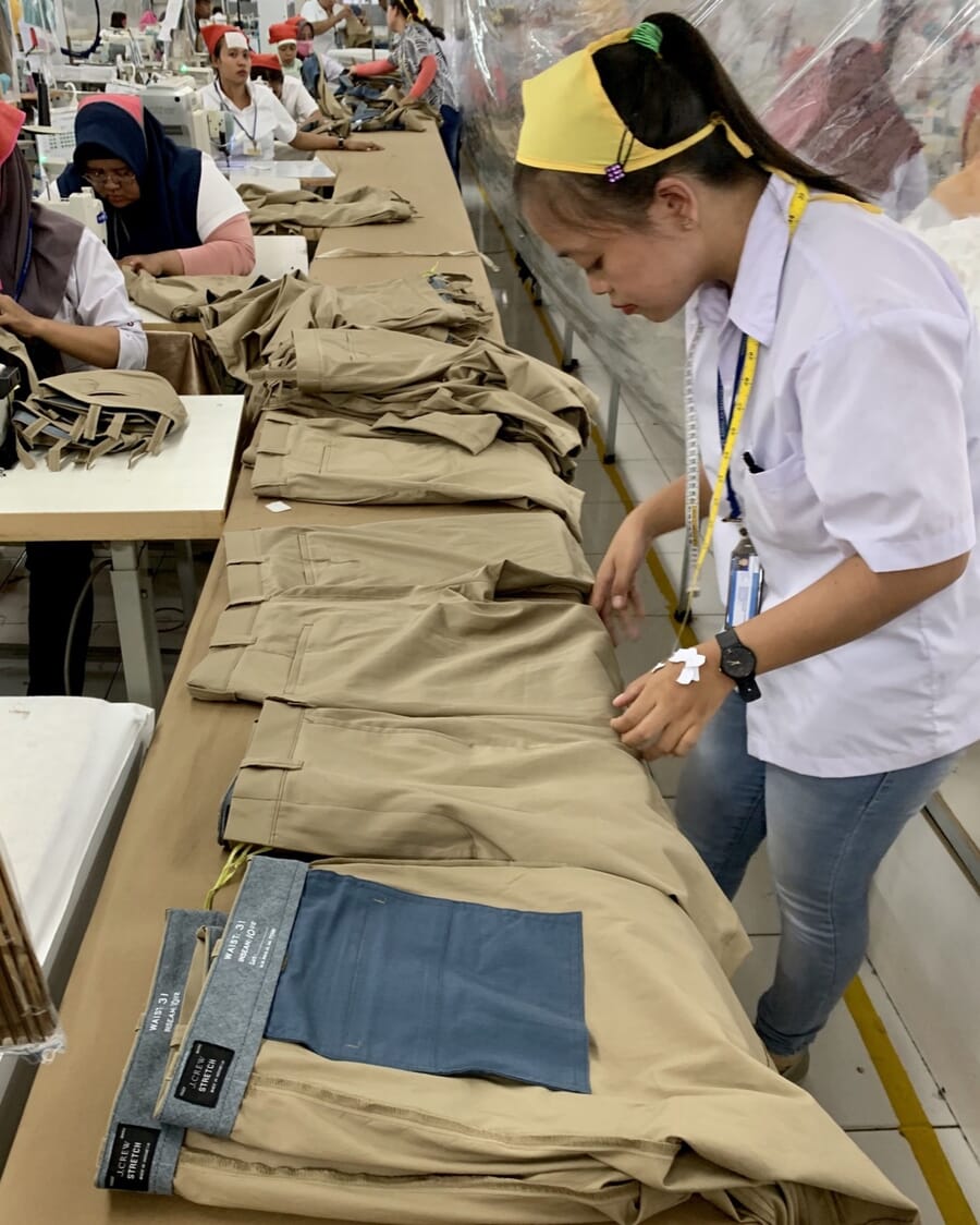 Inspector checking a row of khaki trousers laid flat on a long table