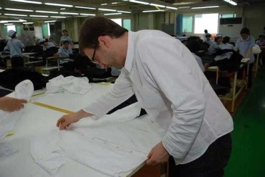 Man measuring a white shirt laid out on a table with a tape
