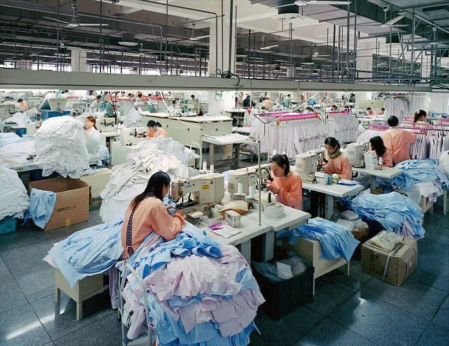 Operators sewing light blue and pink shirts with cut pieces in boxes beside them