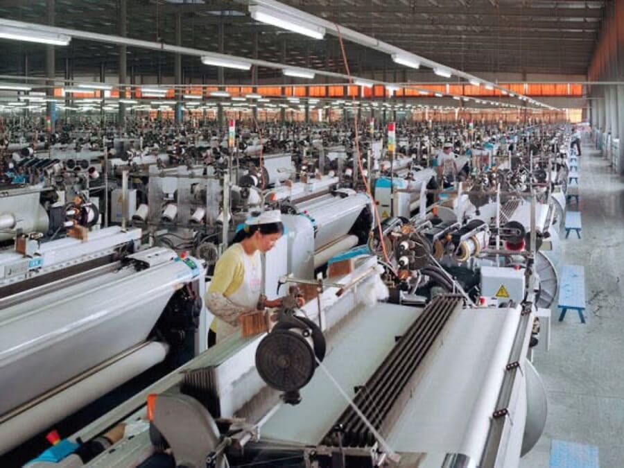 Rows of weaving looms producing white fabric in a large mill hall