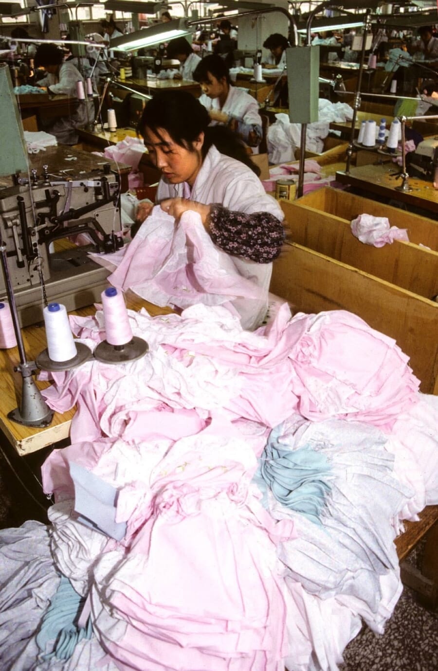 Operator working through a pile of pink knit garments at her machine