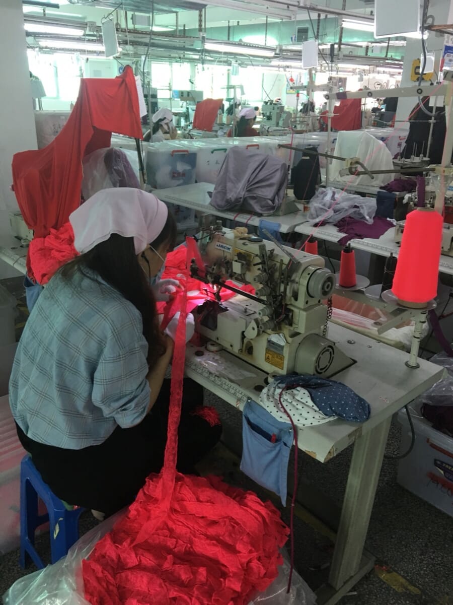 Operator at an overlock machine with a bundle of red knit fabric beside her