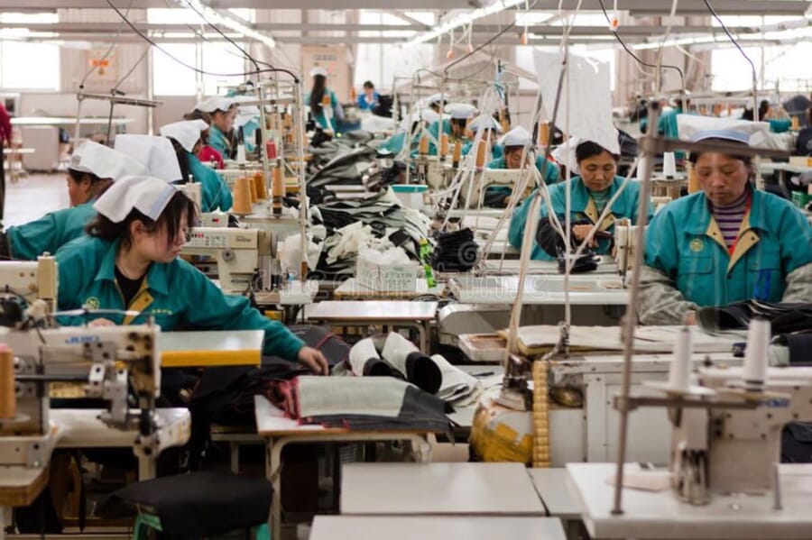 Operators in green smocks and caps along a line of sewing machines