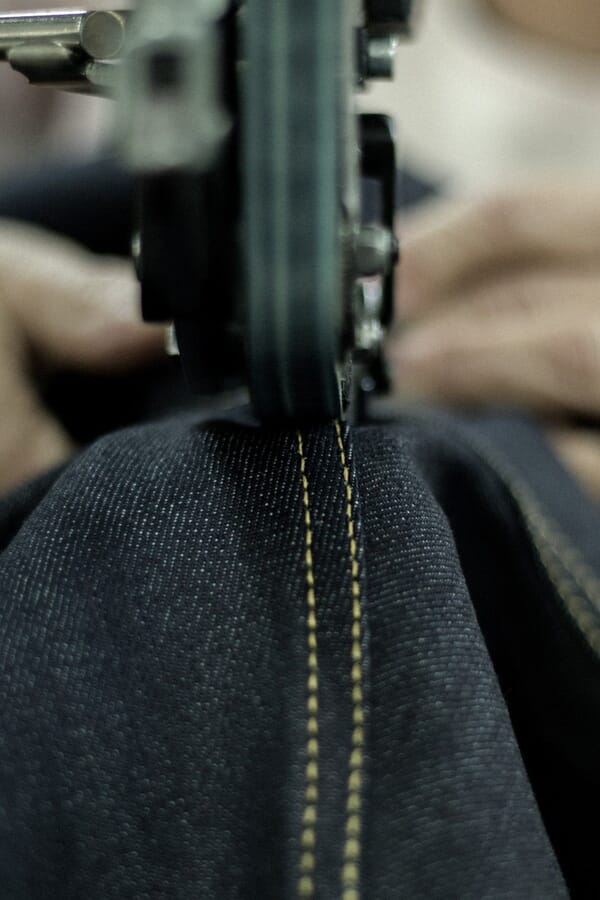 Close-up of a machine topstitching a dark denim seam