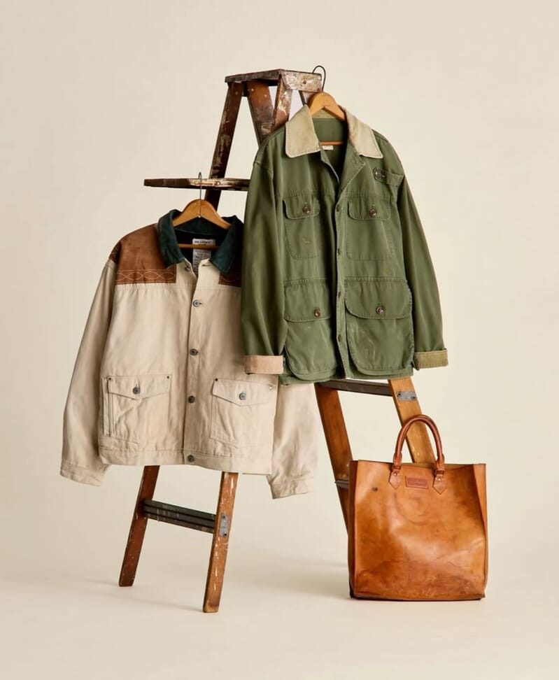 Two utility jackets hung on a wooden ladder with a leather tote