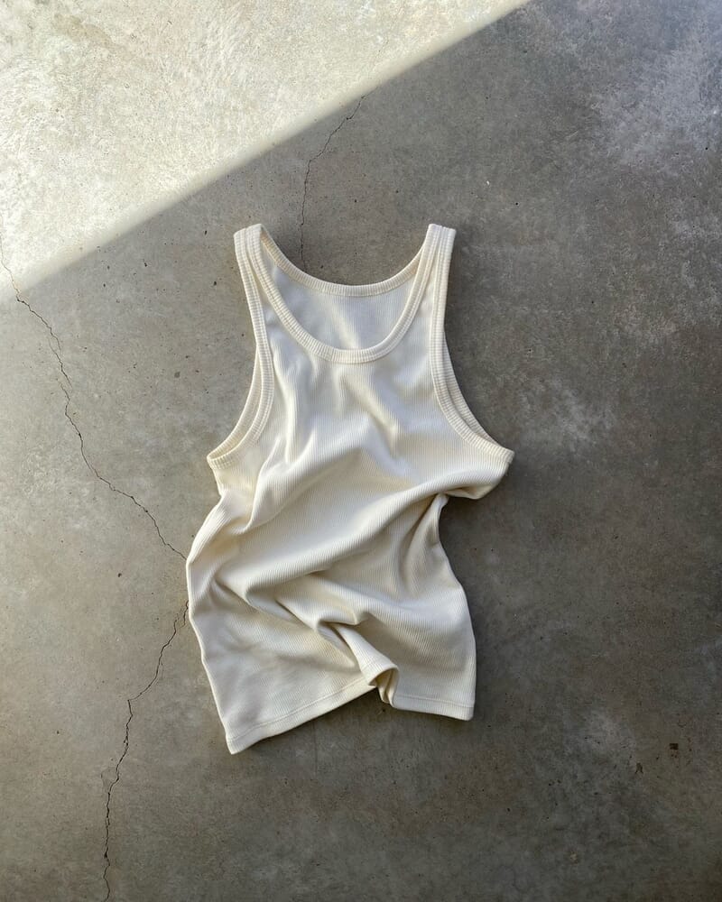A cream ribbed tank top laid flat on a concrete floor
