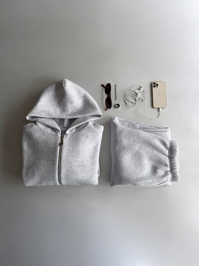 A grey fleece zip hoodie and matching joggers folded flat on a light grey floor