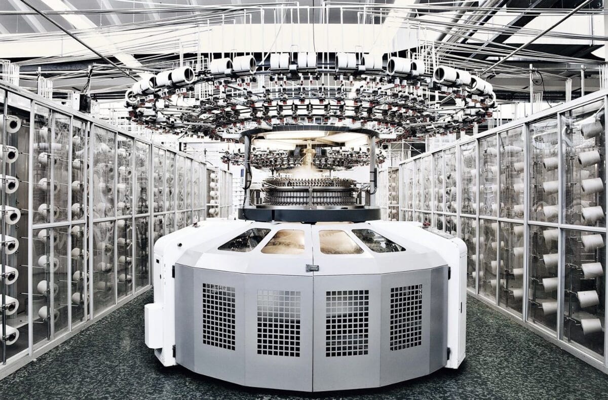 Large circular knitting machine with yarn cones on racks around it