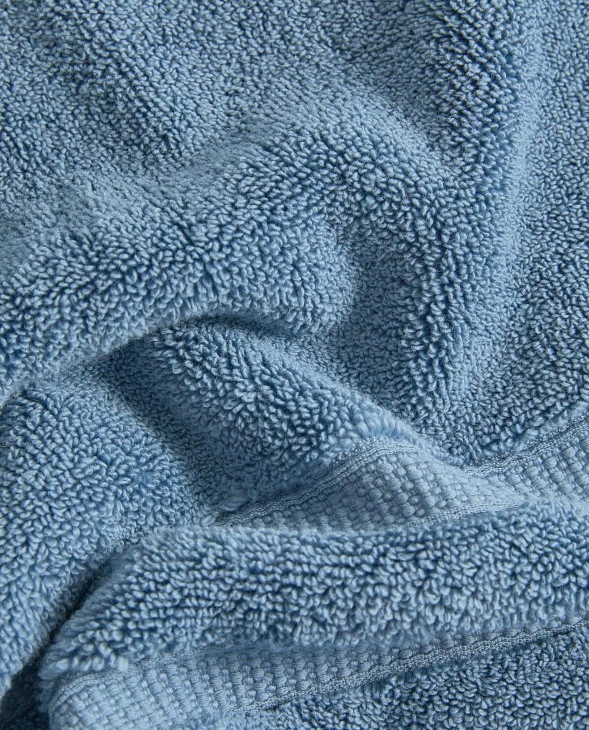 Blue cotton terry bath towel showing the loop pile and the stitched hem